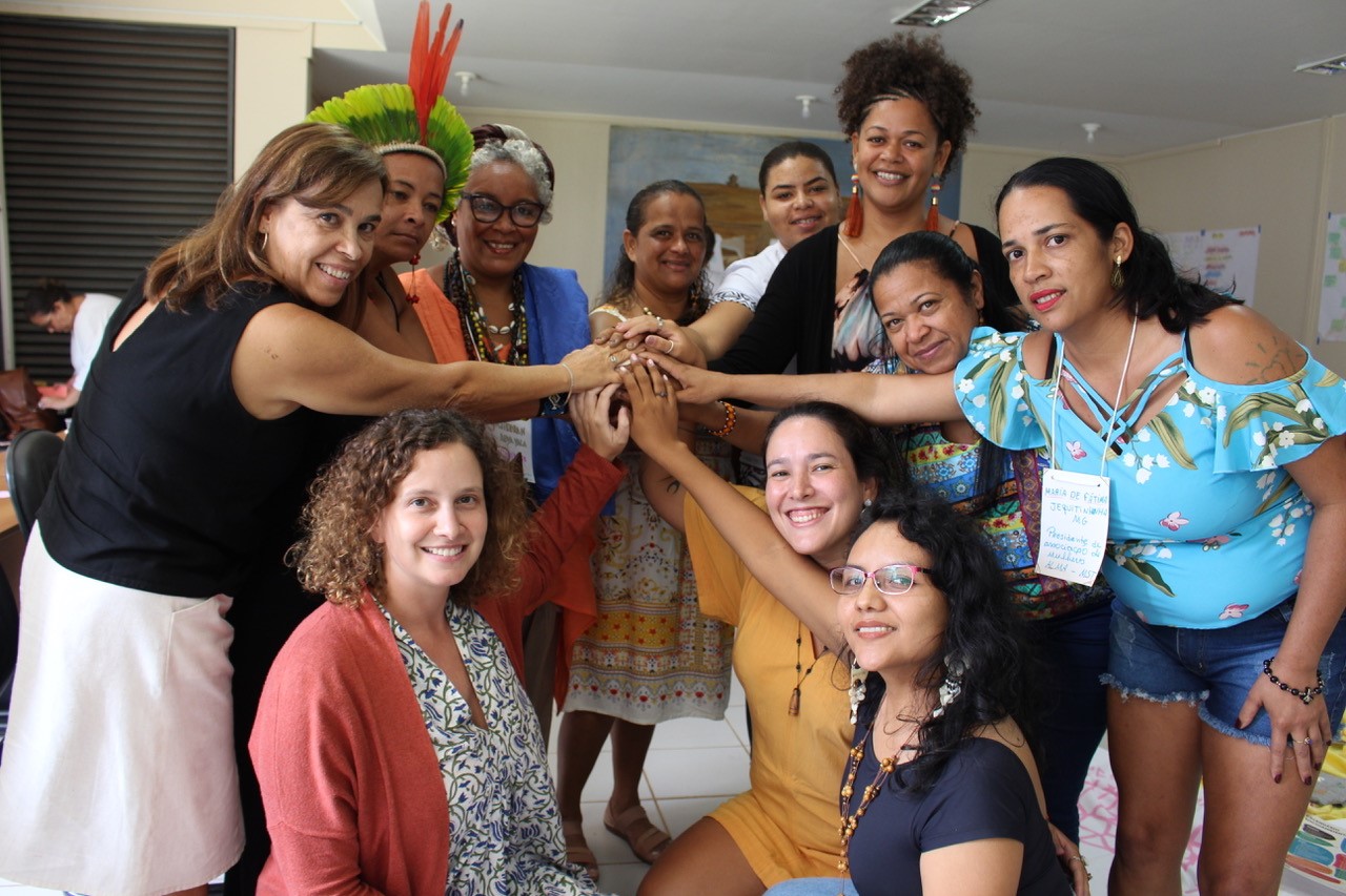 A photo of eleven women in Brazil posing together for the camera. They are leaning in so that their hands are touching, and many of them are smiling.